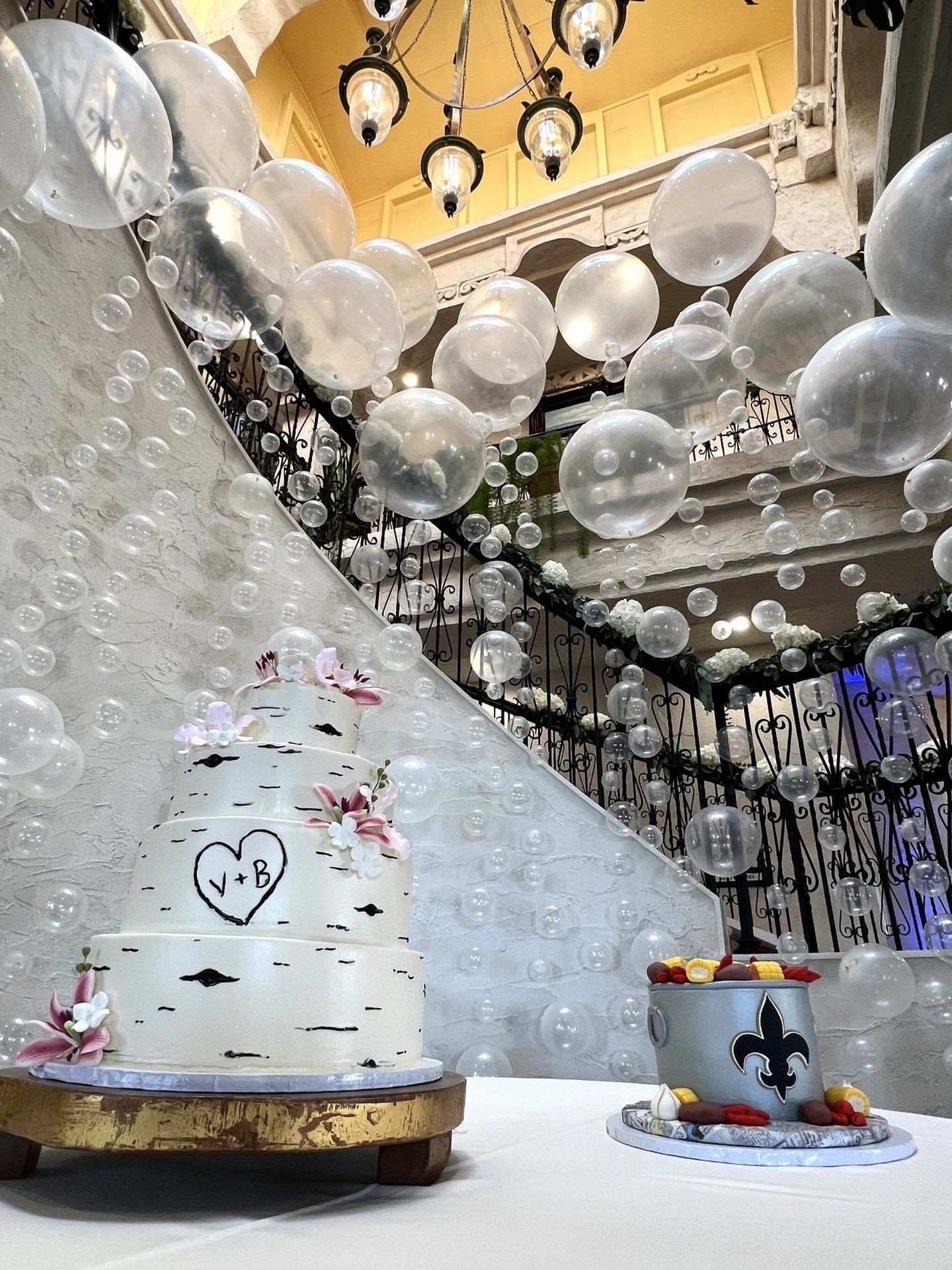 Wedding cake with floral decorations in front of staircase adorned with hanging clear bubbles.