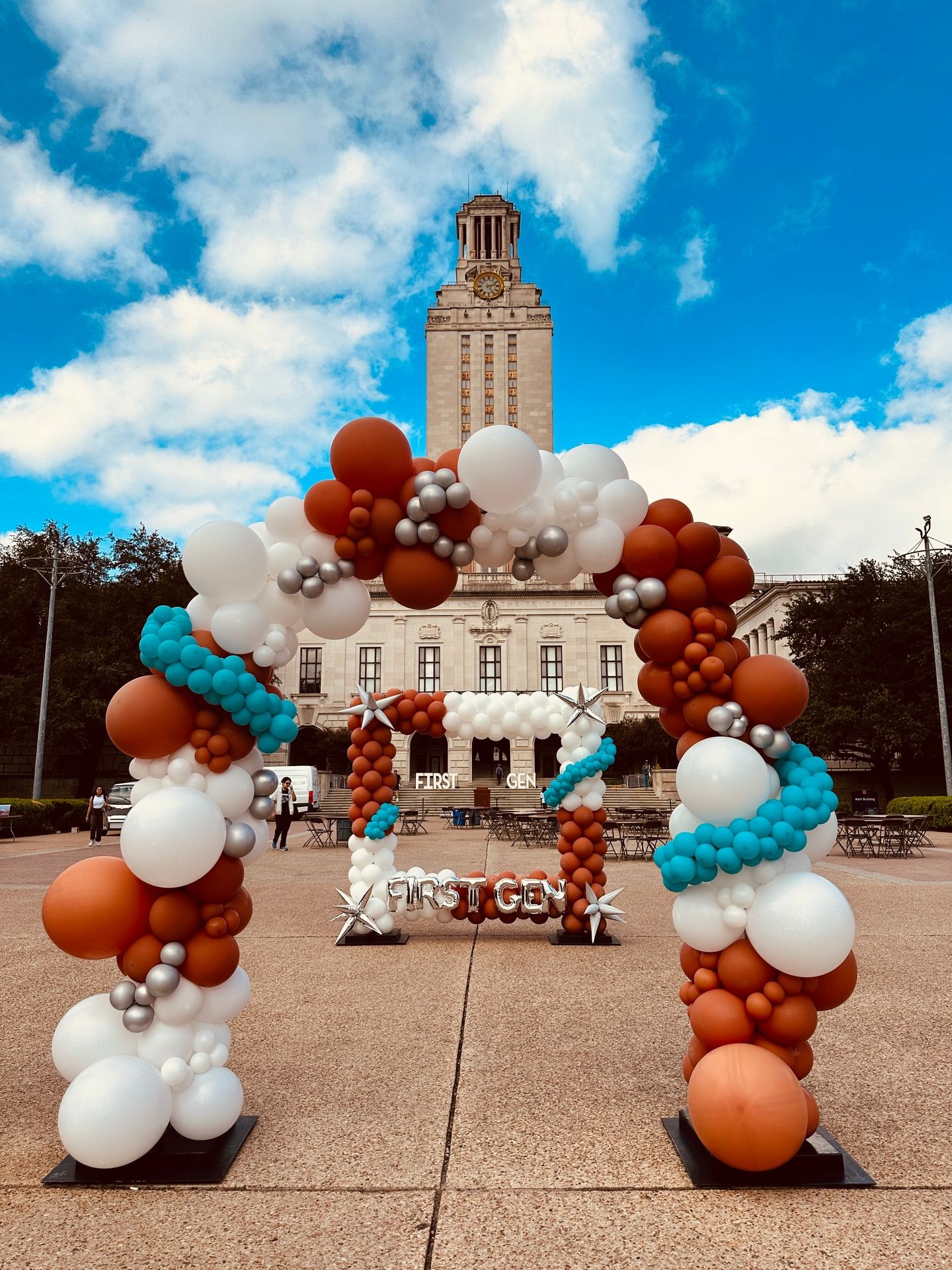 Colorful balloon archway on a university plaza with a clock tower in the background.