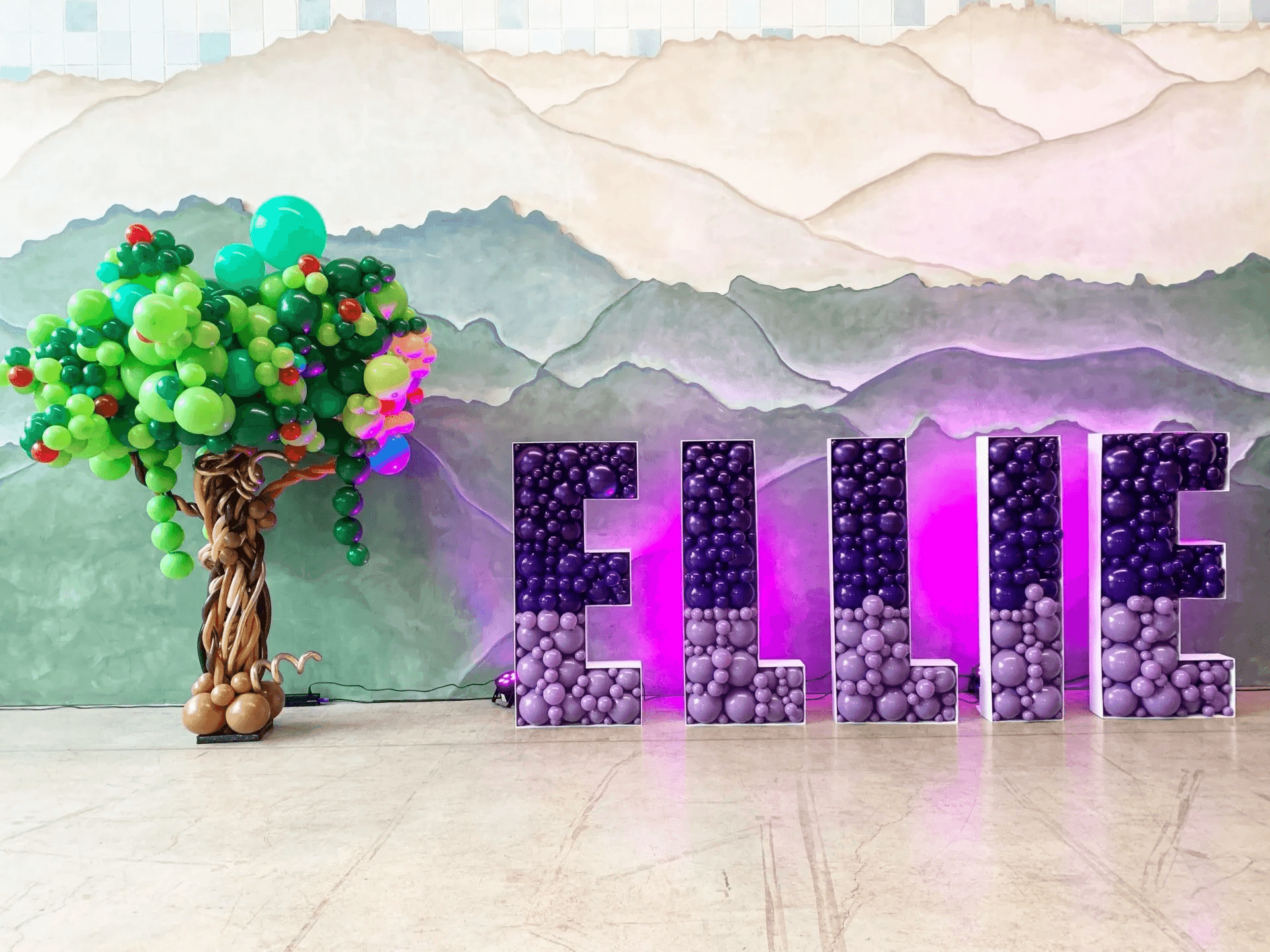 Balloon tree and balloon letters spelling 'ELLIE' against a mural backdrop.